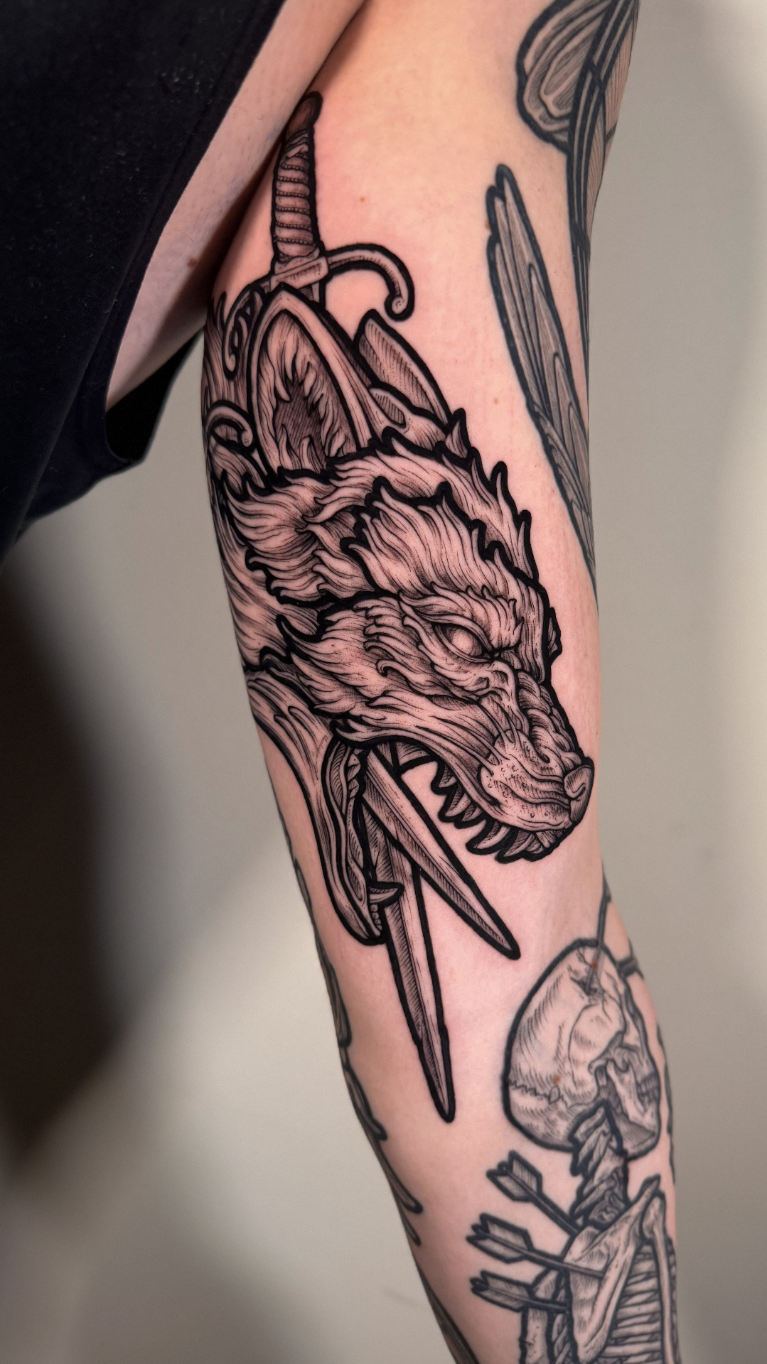 Engraving-style wolf and dagger tattoo on the arm